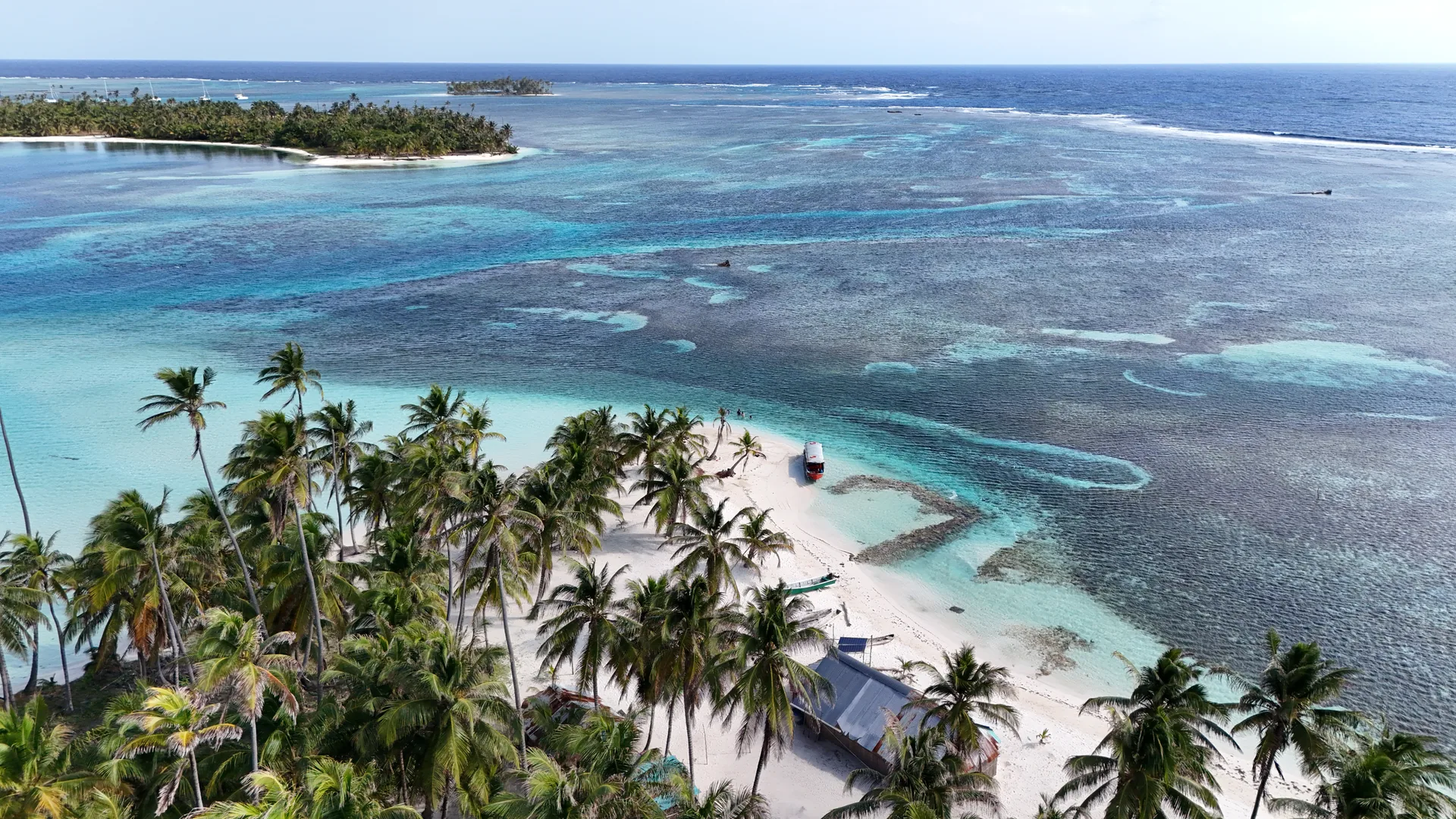 Aerial view of palm-lined white-sand islands, boats and turquoise reef water in the San Blas Islands.