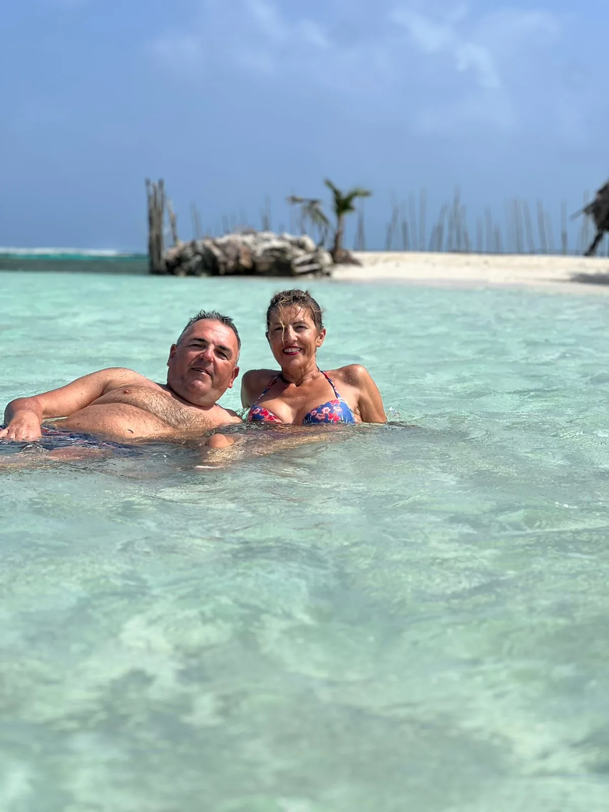 Two visitors relaxing in clear turquoise water beside a sandy shore in the San Blas Islands.