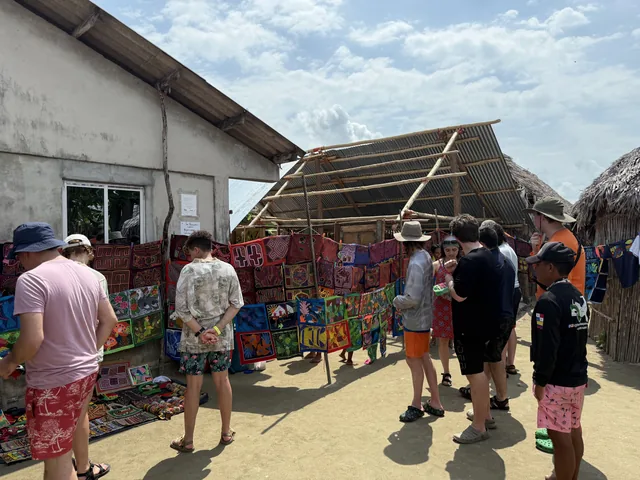 Visitors browsing colorful patterned textile panels and bracelets at an outdoor stall in Guna Yala, Panama.