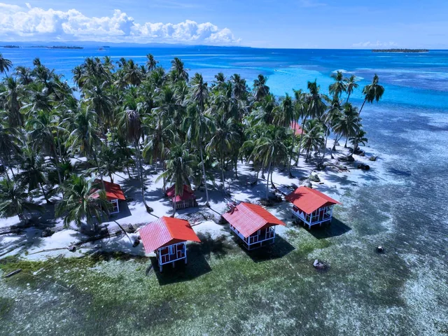 Aerial view of red-roofed cabins beside a palm-covered shore on Yanis Island in Panama’s San Blas Islands.