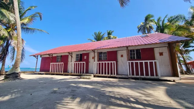 Red-roofed group cabin with white veranda railings beneath coconut palms on Yanis Island in San Blas, Panama.