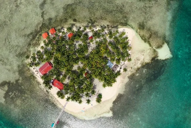 Overhead view of Yanis Island’s sandy shoreline, coconut palms, red-roofed cabins and wooden pier in San Blas.
