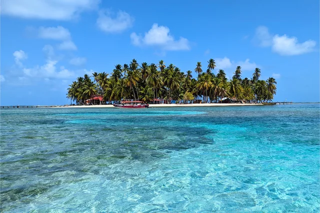 Palm-covered Yanis Island beyond clear turquoise water, with a small boat beside the beach in San Blas, Panama.